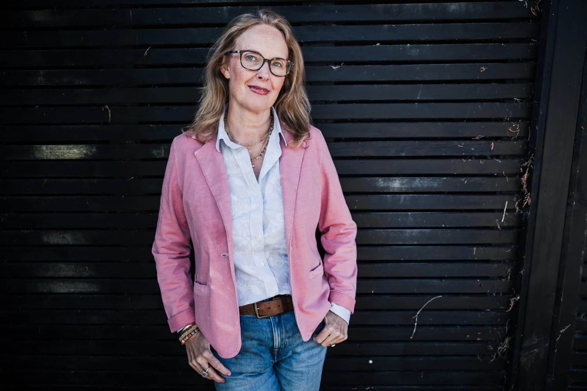 Cara Cunniff in a pink blazer, looking at the camera against a dark wall